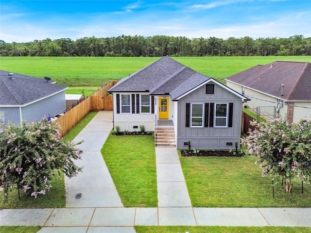 view of front of property with a shingled roof, fence, crawl space, board and batten siding, and a front yard