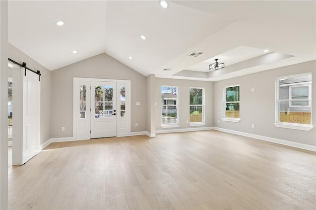 unfurnished living room featuring lofted ceiling, a barn door, and light hardwood / wood-style flooring