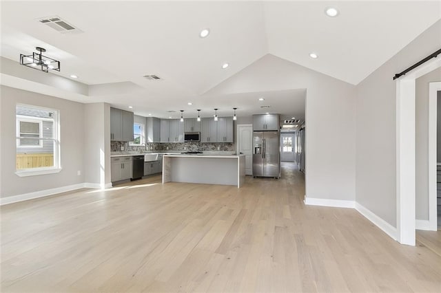 kitchen featuring a center island, appliances with stainless steel finishes, gray cabinets, a barn door, and decorative backsplash