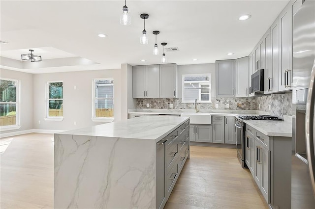 kitchen featuring gray cabinetry, light stone counters, a center island, appliances with stainless steel finishes, and pendant lighting