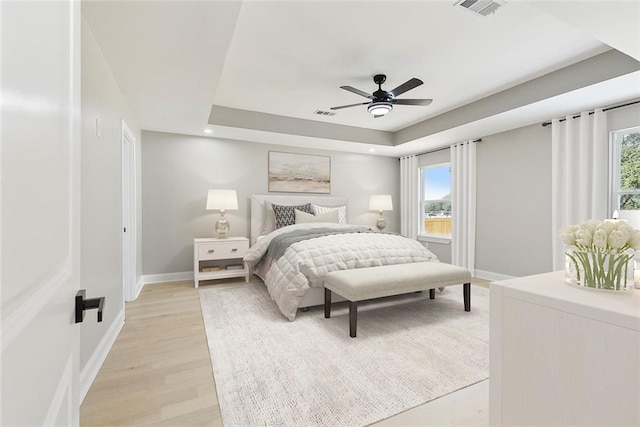 bedroom with ceiling fan, a tray ceiling, and light hardwood / wood-style flooring