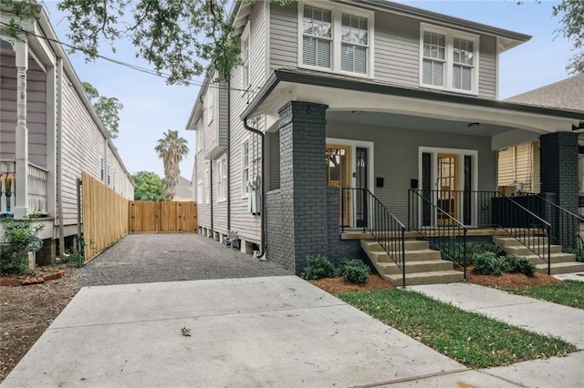 traditional style home featuring driveway, a porch, fence, and brick siding