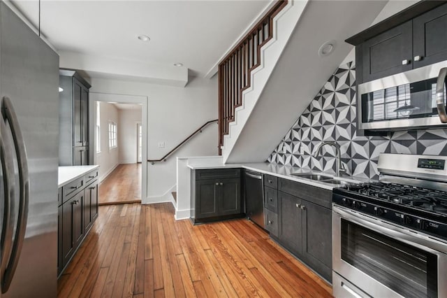 kitchen with sink, tasteful backsplash, appliances with stainless steel finishes, pendant lighting, and light hardwood / wood-style floors