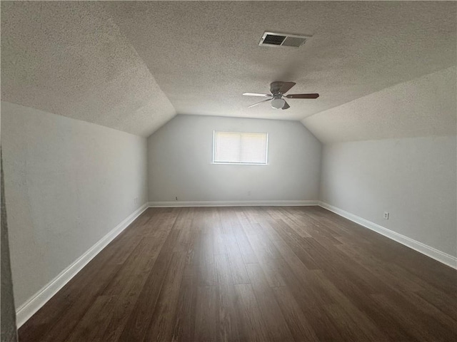 additional living space featuring dark hardwood / wood-style flooring, ceiling fan, lofted ceiling, and a textured ceiling