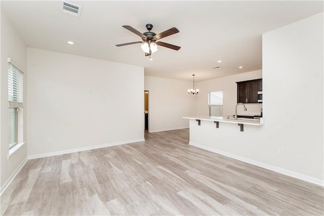 unfurnished living room with sink, ceiling fan with notable chandelier, and light wood-type flooring