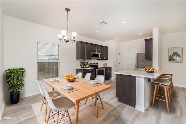 kitchen with pendant lighting, a chandelier, dark brown cabinetry, light hardwood / wood-style floors, and stainless steel appliances