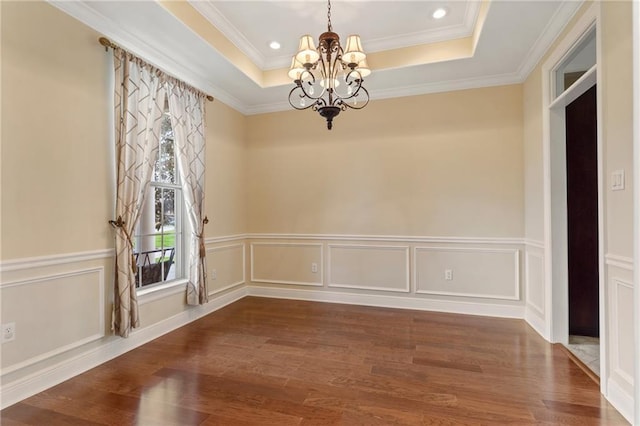 empty room with dark hardwood / wood-style flooring, a tray ceiling, crown molding, and a chandelier