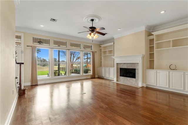 unfurnished living room featuring crown molding, ceiling fan, wood-type flooring, and a tile fireplace