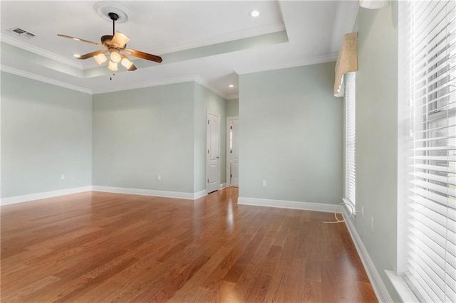 empty room featuring a tray ceiling, wood-type flooring, ornamental molding, and ceiling fan