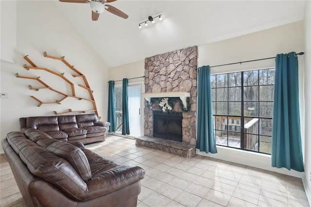 tiled living room with ceiling fan, a stone fireplace, and vaulted ceiling