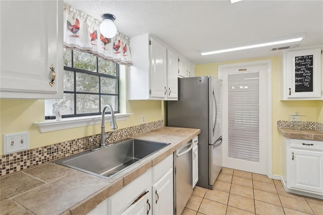 kitchen featuring sink, tile countertops, light tile patterned floors, appliances with stainless steel finishes, and white cabinets