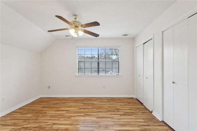 unfurnished bedroom featuring ceiling fan, lofted ceiling, two closets, and light wood-type flooring