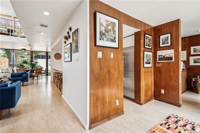 corridor featuring light colored carpet and wood walls