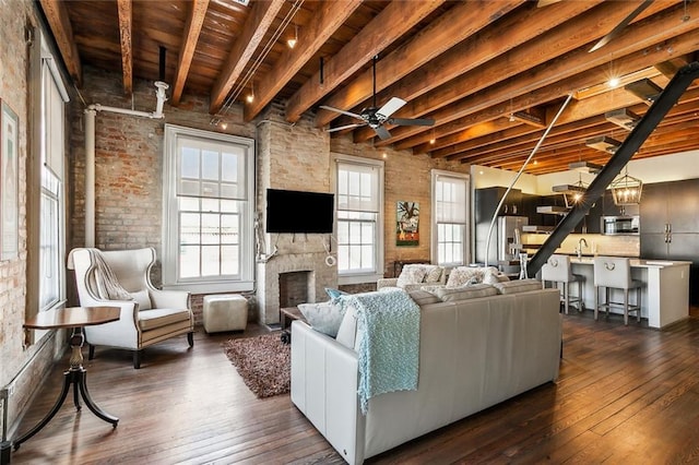 living room featuring sink, beam ceiling, dark hardwood / wood-style flooring, ceiling fan, and a fireplace