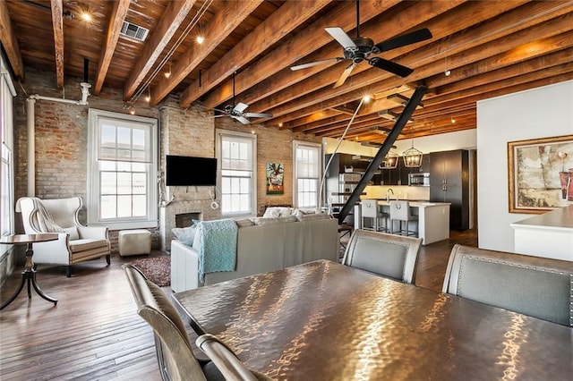 dining space with brick wall, hardwood / wood-style floors, a fireplace, ceiling fan, and beam ceiling