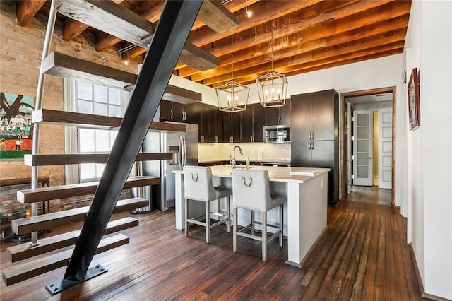 kitchen featuring dark hardwood / wood-style floors, beamed ceiling, decorative backsplash, dark brown cabinets, and a center island with sink