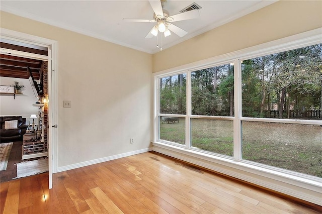 empty room with crown molding, light wood-style flooring, visible vents, ceiling fan, and baseboards