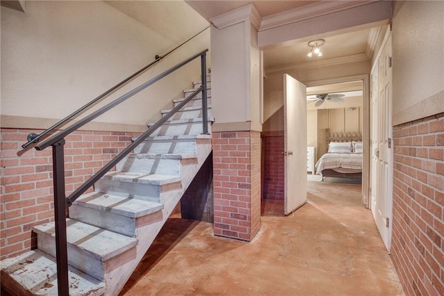 staircase featuring ceiling fan, brick wall, concrete floors, and ornamental molding