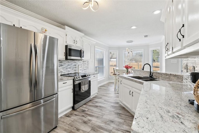 kitchen featuring sink, white cabinetry, hanging light fixtures, ornamental molding, and stainless steel appliances