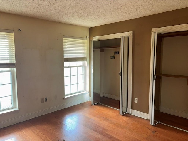 7540 Fieldston Rd, New Orleans, LA 70126 - unfurnished bedroom with wood finished floors, multiple windows, baseboards, and a textured ceiling