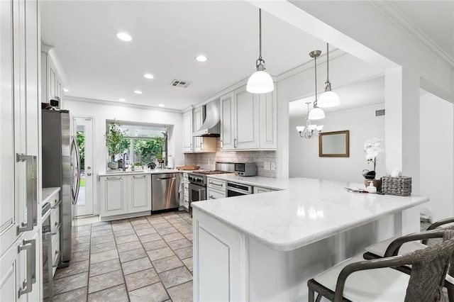 kitchen featuring decorative light fixtures, appliances with stainless steel finishes, kitchen peninsula, wall chimney range hood, and white cabinets