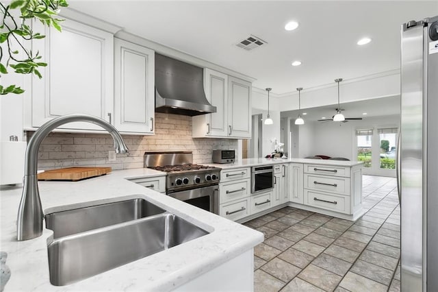 kitchen with sink, stainless steel appliances, decorative light fixtures, kitchen peninsula, and wall chimney exhaust hood