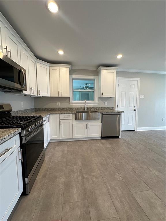 kitchen featuring appliances with stainless steel finishes, white cabinetry, sink, ornamental molding, and light stone counters