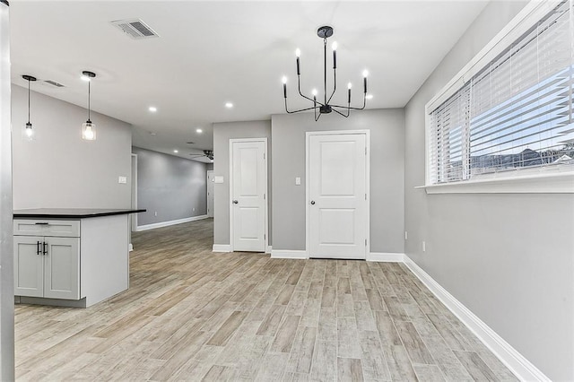 unfurnished dining area with ceiling fan with notable chandelier and light hardwood / wood-style flooring