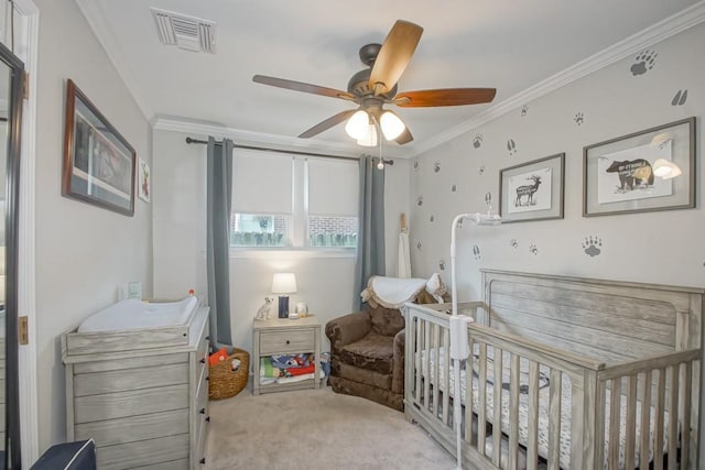 carpeted bedroom with a crib, a ceiling fan, visible vents, and crown molding