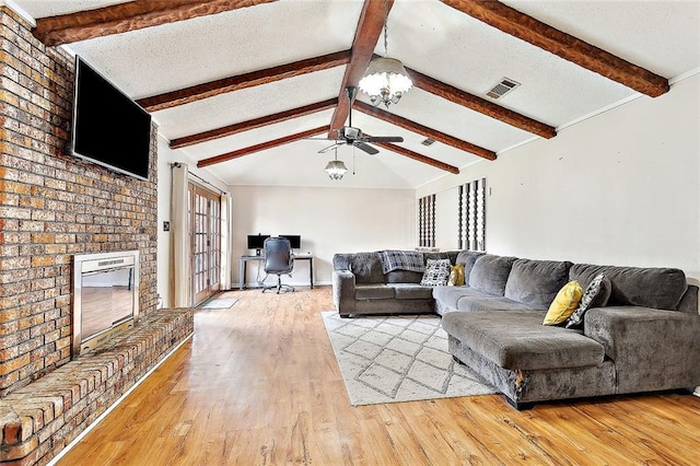 living room featuring vaulted ceiling with beams, a brick fireplace, a textured ceiling, ceiling fan, and light hardwood / wood-style floors