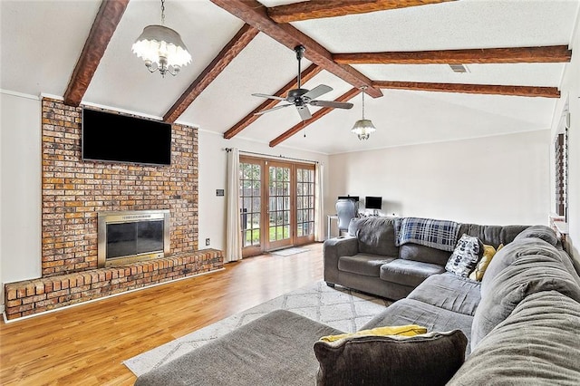 living room with a brick fireplace, vaulted ceiling with beams, ceiling fan with notable chandelier, and light hardwood / wood-style flooring