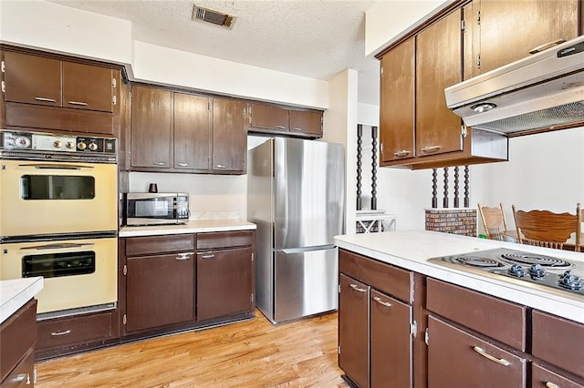 kitchen featuring dark brown cabinetry, stainless steel appliances, light hardwood / wood-style floors, and a textured ceiling