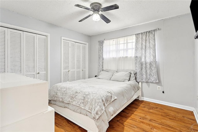 bedroom with ceiling fan, hardwood / wood-style flooring, a textured ceiling, and multiple closets