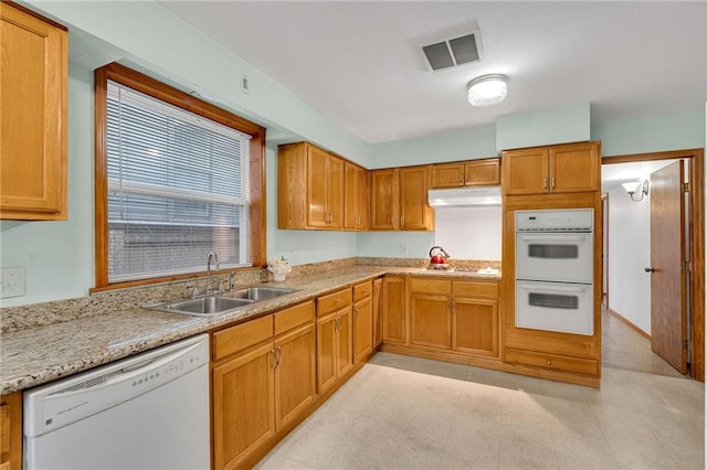 kitchen featuring white appliances, light stone countertops, and sink