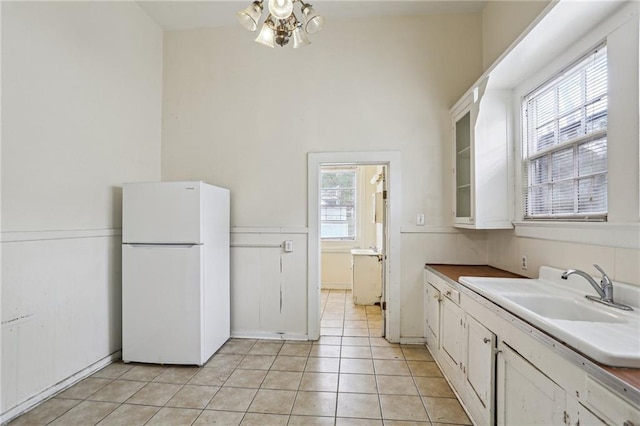 kitchen featuring sink, white refrigerator, a notable chandelier, white cabinets, and light tile patterned flooring