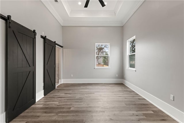 unfurnished bedroom with hardwood / wood-style flooring, ornamental molding, a barn door, and a tray ceiling