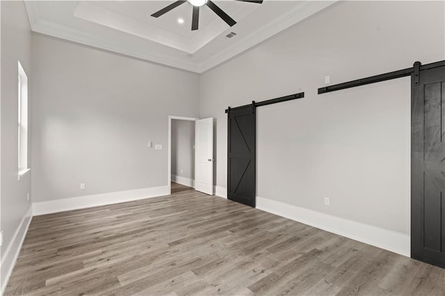 unfurnished bedroom with ornamental molding, a barn door, a raised ceiling, and light hardwood / wood-style floors