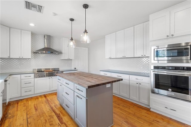 kitchen featuring white cabinets, appliances with stainless steel finishes, wooden counters, and wall chimney range hood