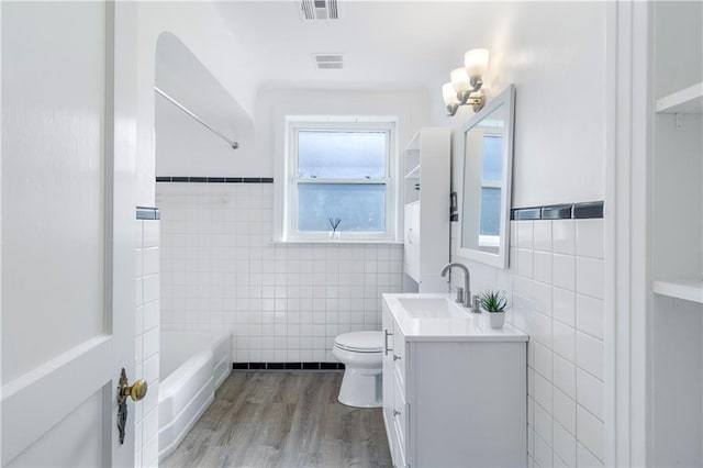 full bathroom featuring hardwood / wood-style floors, tile walls, vanity, toilet, and washtub / shower combination