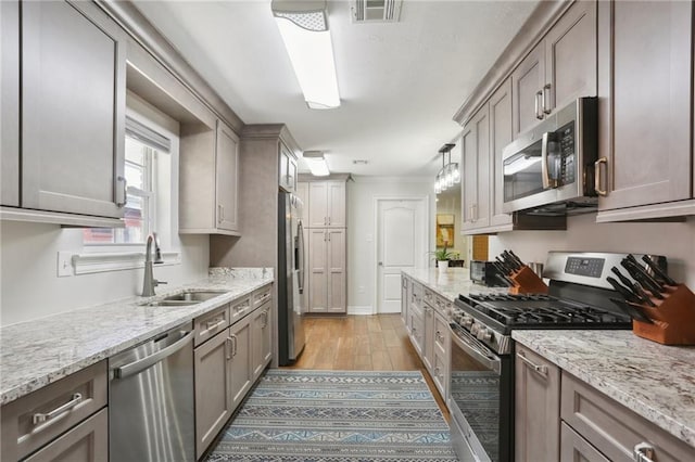 kitchen featuring sink, light stone counters, decorative light fixtures, stainless steel appliances, and light hardwood / wood-style floors