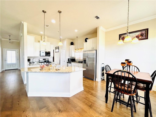 kitchen with light stone countertops, white cabinetry, appliances with stainless steel finishes, and a kitchen island with sink