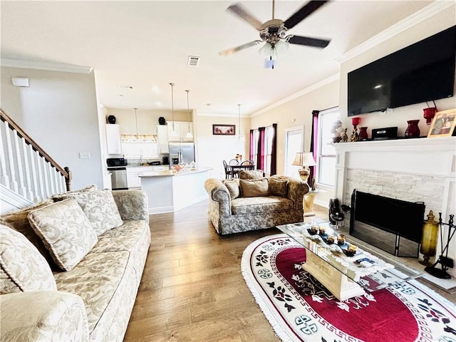 living room featuring crown molding, a stone fireplace, hardwood / wood-style floors, and ceiling fan