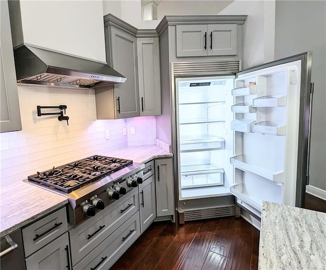 kitchen with stainless steel gas stovetop, light stone countertops, gray cabinets, and wall chimney range hood