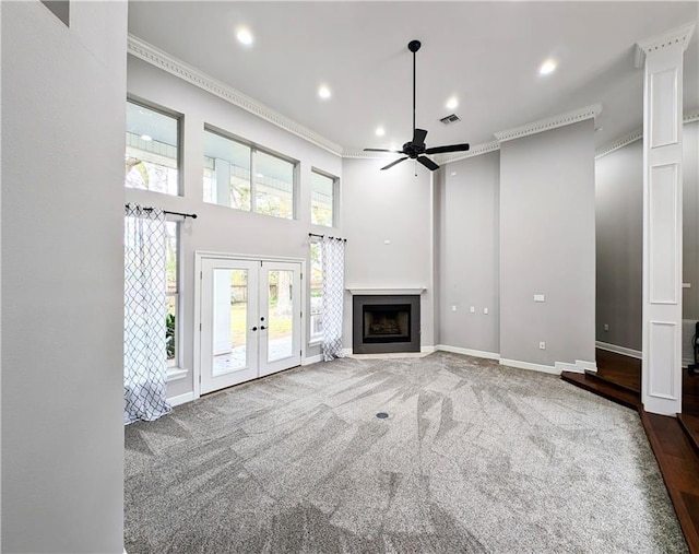 unfurnished living room featuring carpet floors, a high ceiling, ceiling fan, crown molding, and french doors