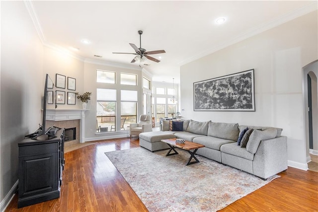 living room featuring ceiling fan, ornamental molding, dark hardwood / wood-style floors, and a tile fireplace