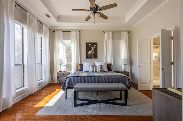 bedroom with multiple windows, crown molding, hardwood / wood-style floors, and a tray ceiling