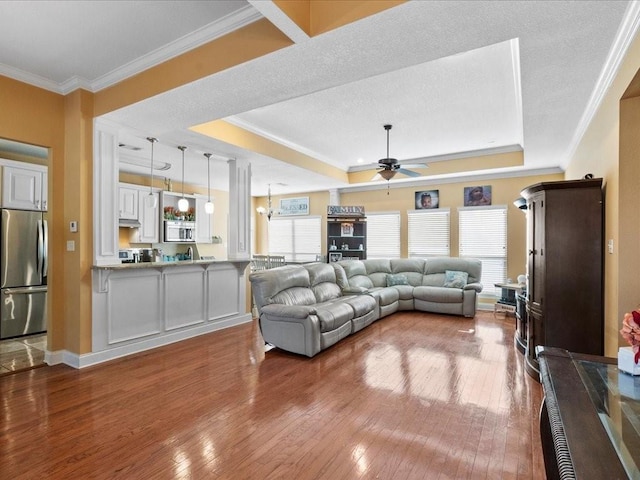 living room featuring a raised ceiling, wood-type flooring, ceiling fan, and crown molding