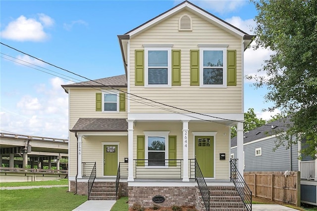 view of front of house featuring a porch, roof with shingles, a front yard, and fence