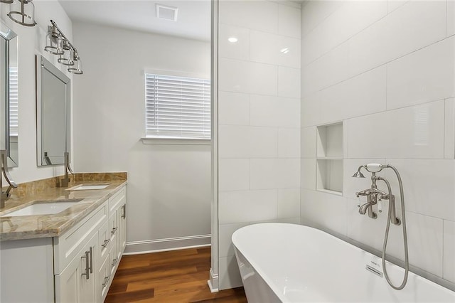 bathroom featuring double vanity, a soaking tub, wood finished floors, and a sink