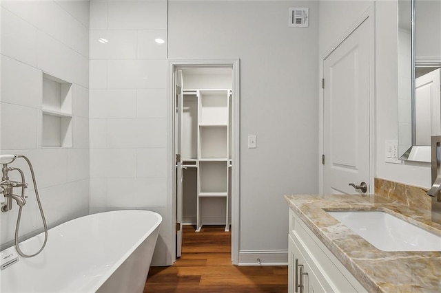 bathroom with visible vents, tile walls, wood finished floors, a soaking tub, and vanity